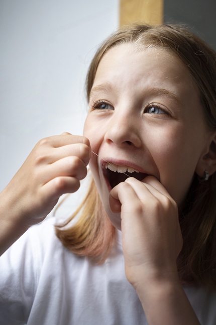 foto de criança, menina, usando fio dental para limpar os dentes