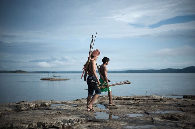 foto de Dois garotos Munduruku caminham ao longo de um rio segurando lanças, remete a matéria 10 motivos para agir pela Amazônia