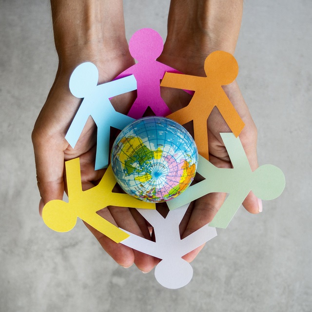 foto mostra um globo terrestre entre as mãos em formato de concha, cercados por formato de pessoas em papel de várias cores simbolizando diversidade, igualdade e inclusão
