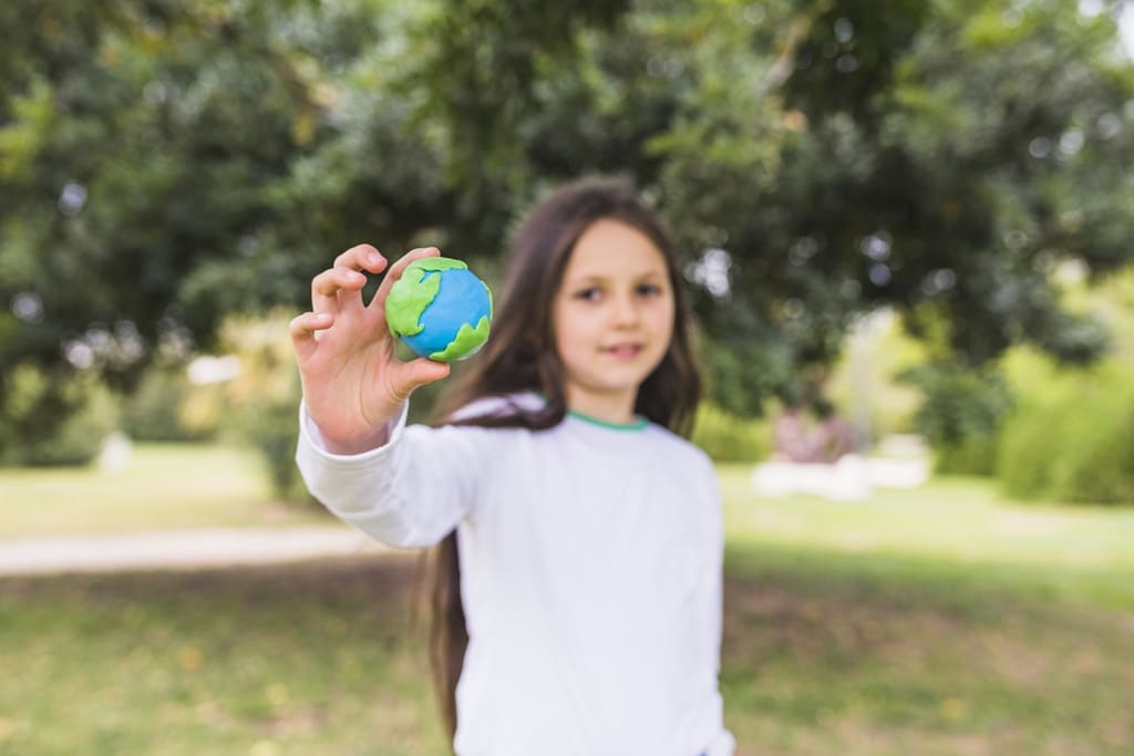 foto de menina criança segurando um globo terrestre pequeno no dedo, remete ao artigo Dia Mundial da Educação Ambiental: Se 
eles semeiam desesperança, nós plantamos sonhos
